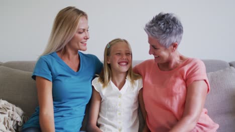 Portrait-of-caucasian-grandmother,-mother-and-daughter-smiling-while-sitting-on-the-couch-at-home