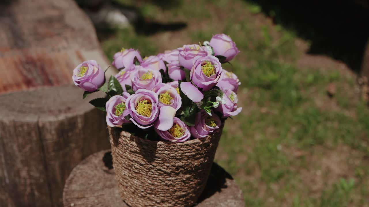 pink flowers in woven basket resting on tree stump in natural light