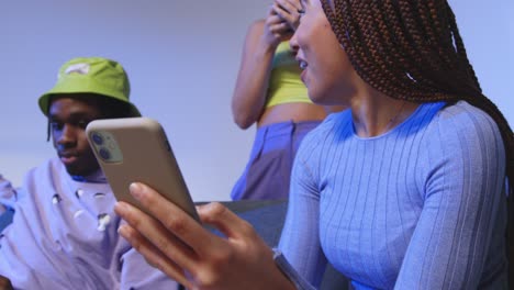 close up studio shot of young gen z friends sitting on sofa sharing social media post on mobile phones