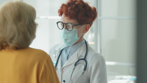 doctora con máscara escuchando al paciente en la clínica