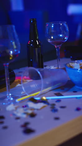 vertical video close up of messy table covered with empty wine glasses beer bottles and snacks at house party 1