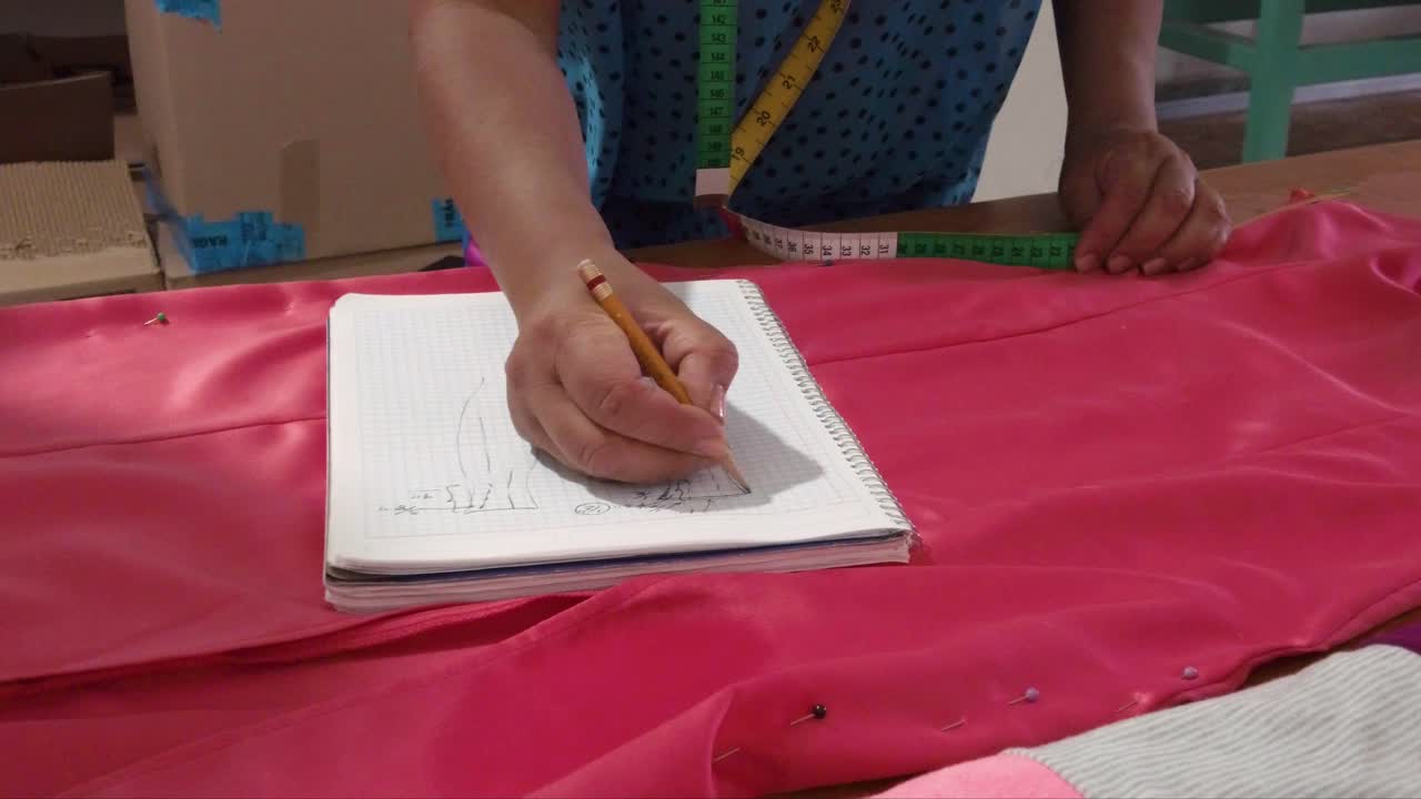 Latin fashion designer taking measures of a dress on a wooden table taking notes