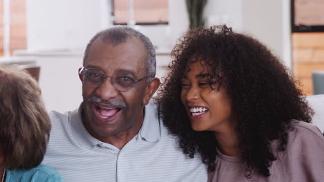 Grandparents-with-teen-and-young-adult-grandchildren-sitting-at-home-laughing-to-camera,-close-up