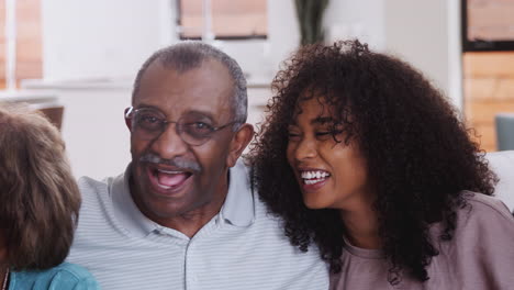 grandparents with teen and young adult grandchildren sitting at home laughing to camera, close up