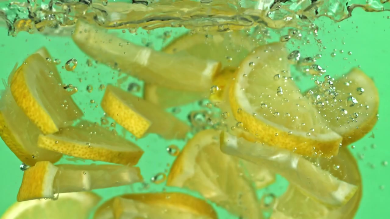 Fresh Lemon Slices Dropping into Water with Bubbles on Green Screen