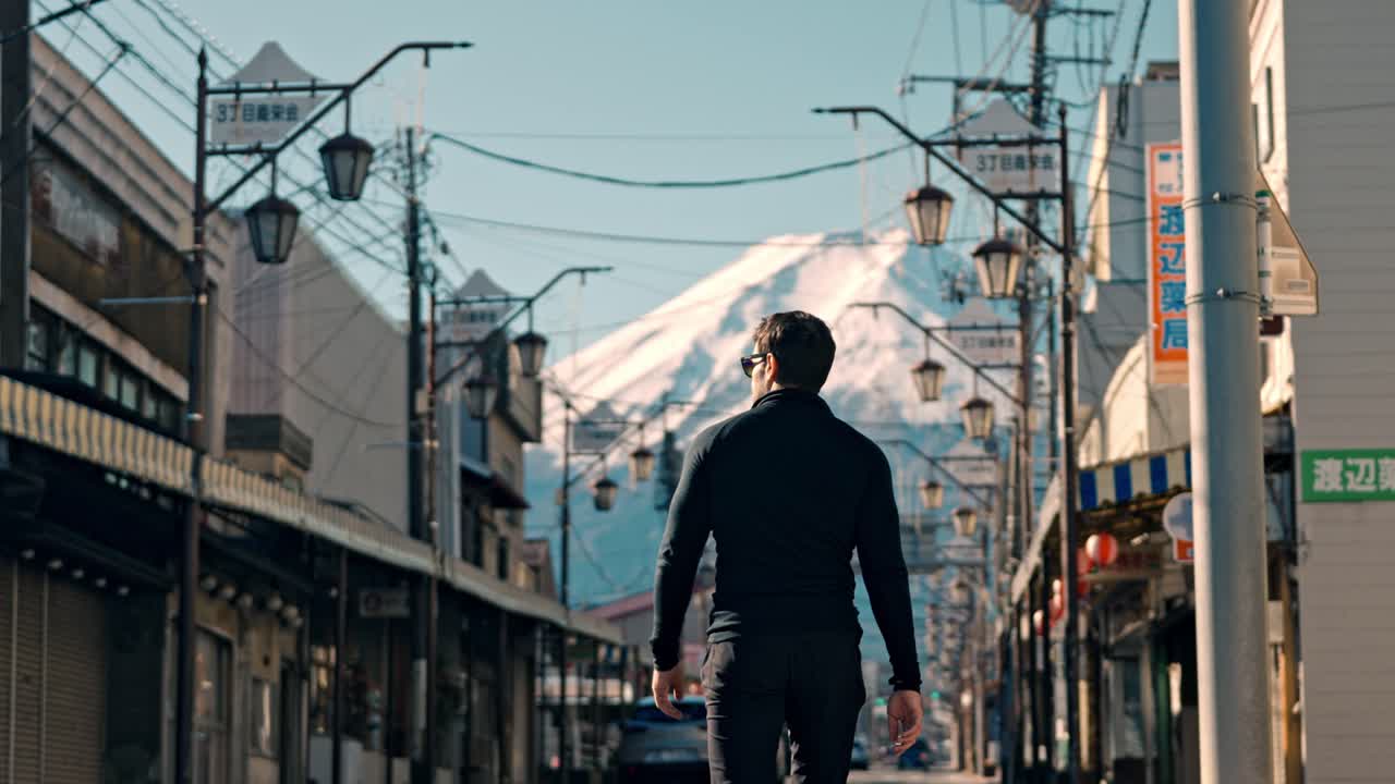 This video clip captures a man walking through Honcho Street in Shizuoka City, with the stunning, snow-covered Mount Fuji looming in the background.