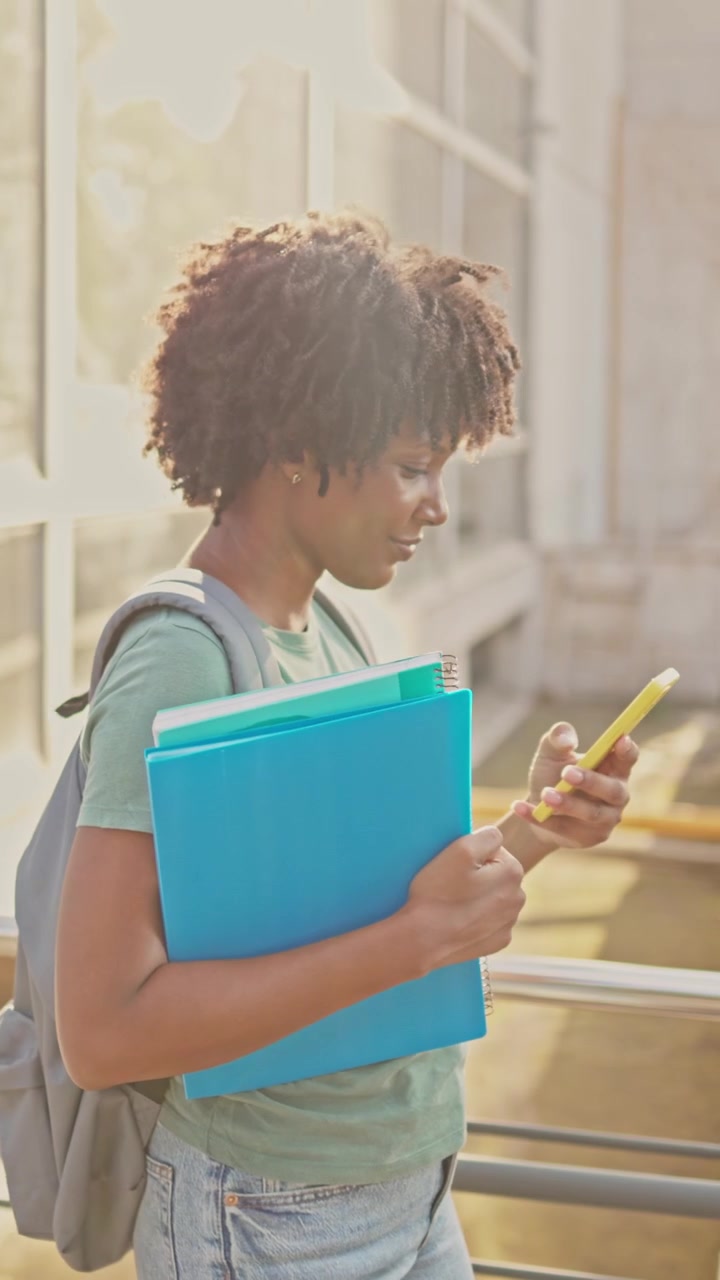 Smiling African American Student Holding Books and Using Smartphone Outdoors