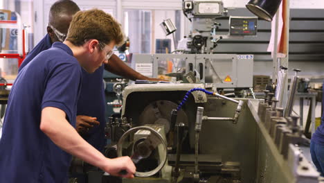 engineer showing teenage apprentice how to use lathe