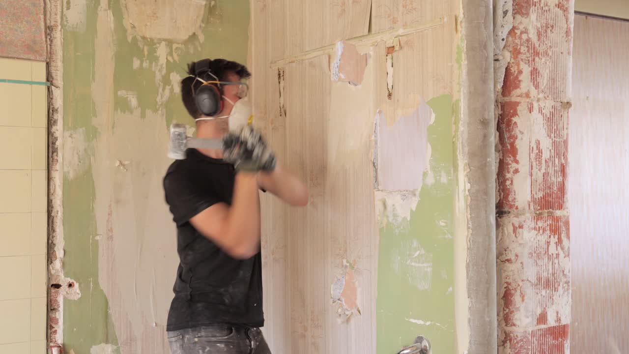 Giovane uomo pratica un foro in un muro con una piccola mazza durante una ristrutturazione.