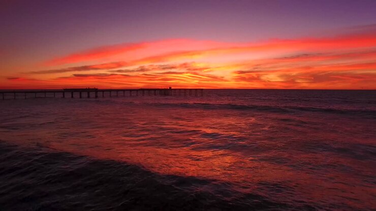 Aerial 4K seascape horizon view of Ocean Beach pier silhouette during a colorful golden orange sunset