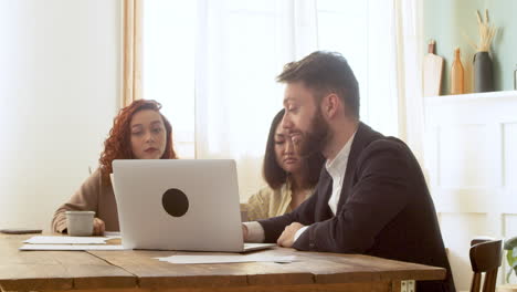 Multiethnisches-Geschäftsteam,-Das-Am-Tisch-Sitzt-Und-Eine-Debatte-Führt,-Während-Es-Auf-Den-Laptop-Computer-1-Schaut