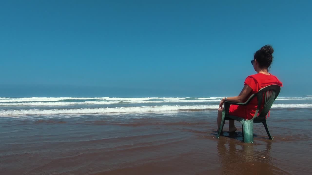 Girl sitting on the beach of Casablanca - filmed from the side, girl centered in the right end of the frame.