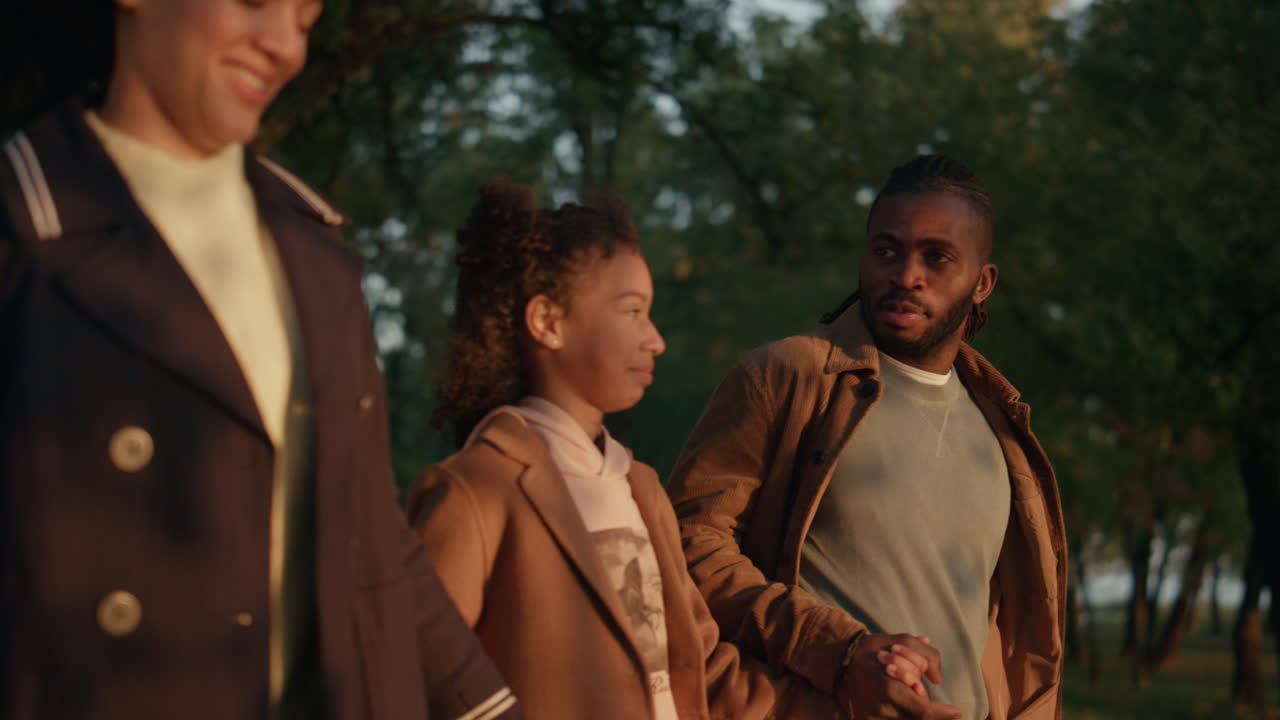 Couple tenant la main de leur fille et souriant dans un parc au coucher du soleil d'automne. Moment familial joyeux.