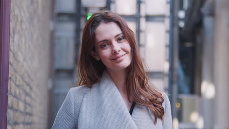 Young-adult-white-businesswoman-standing-on-the-street-smiling-to-camera,-focus-on-foreground,-close-up