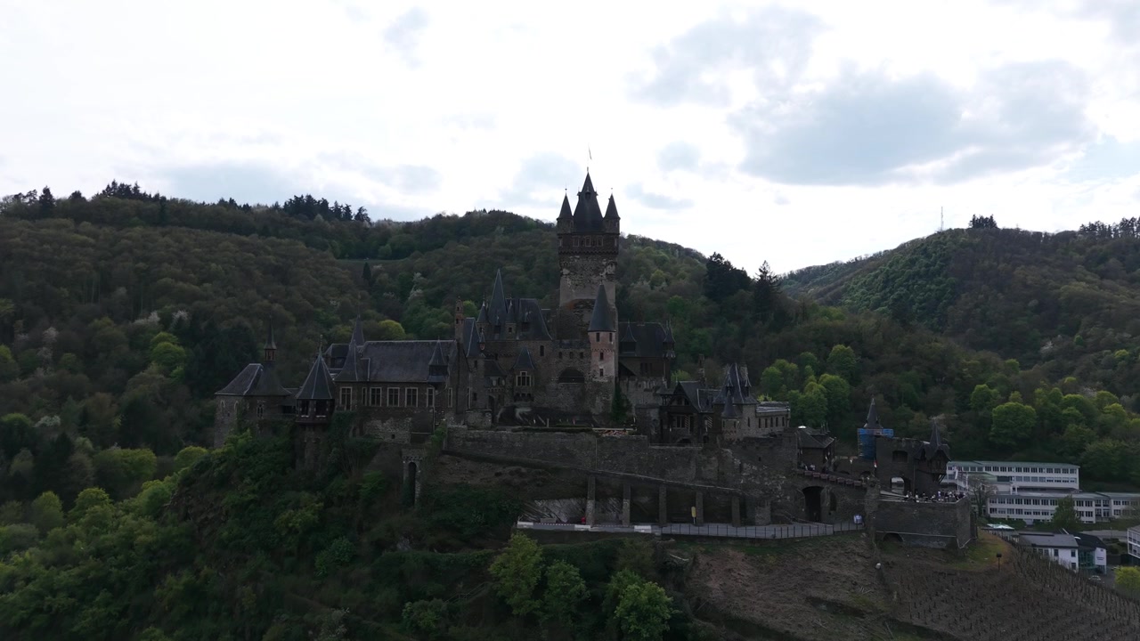 Reichsburg Cochem sijaitsee metsäisellä kukkulalla ympäröivien laaksojen yläpuolella, kun ilmakuva hitaasti loittonee.
