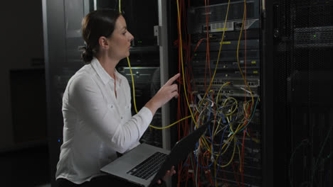 caucasian female it technician using laptop, pointing and checking computer server