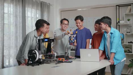 asian man with a laptop and 3d printing explaining about how to use a cyborg hand to the boys at school