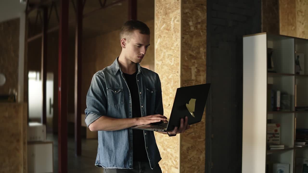 un atractivo joven hombre de negocios concentrado camina con una laptop negra en la mano y escribe