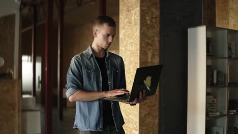 attractive concentrated young business man is walking with black laptop in his hand and typing