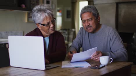 Feliz-Pareja-De-Raza-Mixta-Senior-Haciendo-Papeleo-Y-Usando-Una-Computadora-Portátil