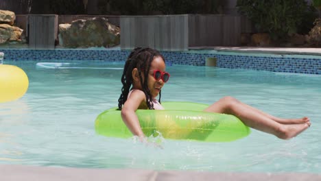 feliz niña afroamericana con gafas de sol flotando en un anillo inflable en la piscina