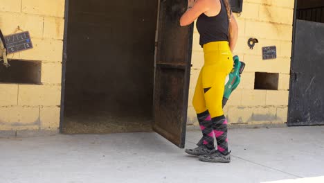 low angle scene of a worker closing a stall door then blowing straw during stable upkeep