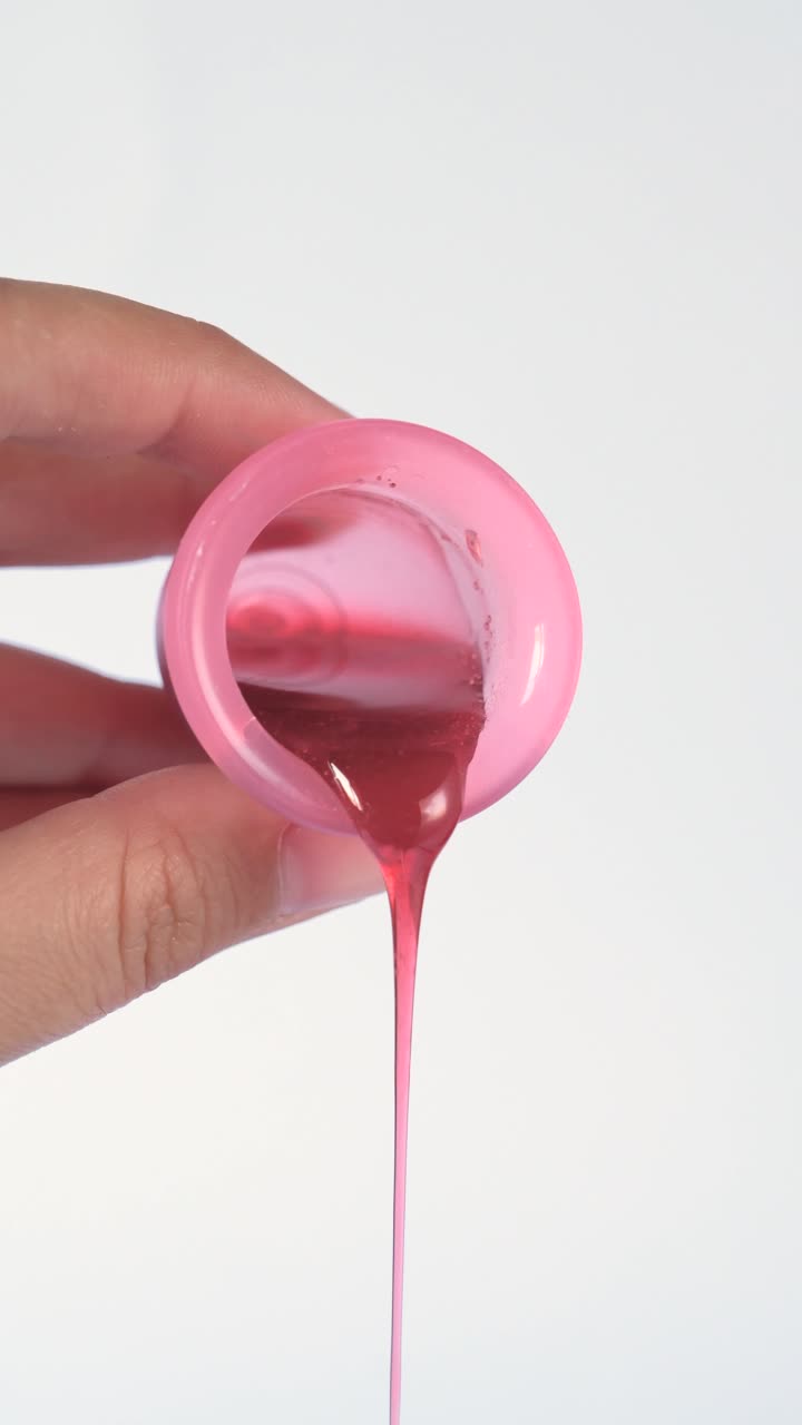 Hand emptying a pink menstrual cup with red liquid, isolated on a white background