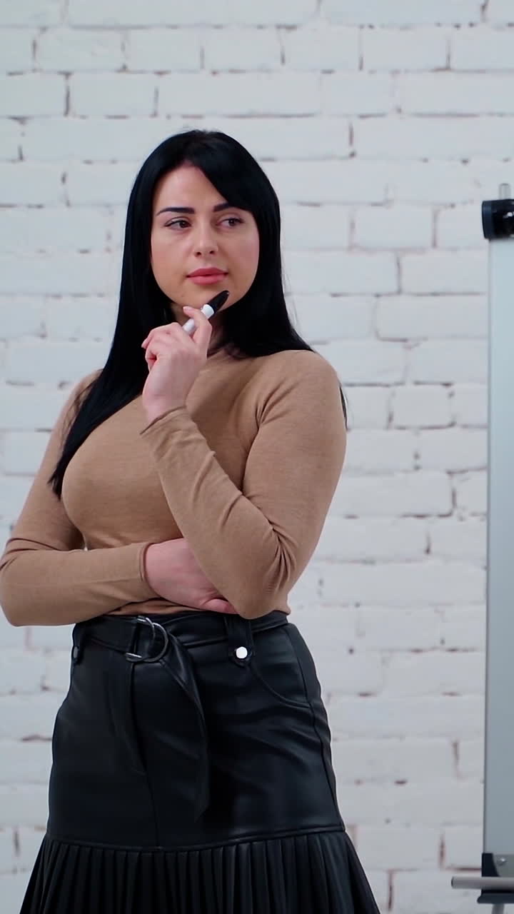 Portrait of a thoughtful businesswoman. Beautiful young female standing with a marker near the board and thinks about new ways in business. Vertical video