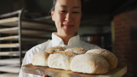 animation of happy asian female baker holding board with fresh baked bread