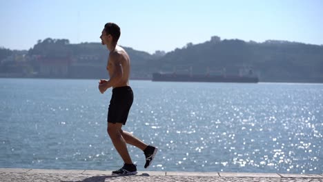 Shirtless-sportsman-running-on-pavement-at-riverside