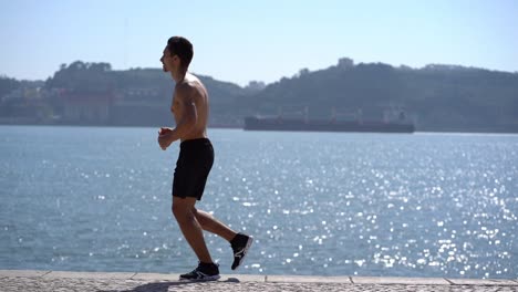 shirtless sportsman running on pavement at riverside