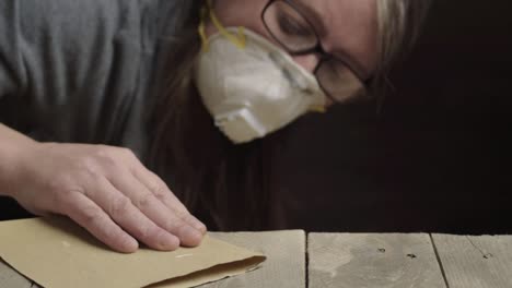 mujer lijando madera mientras usa una máscara protectora al atardecer