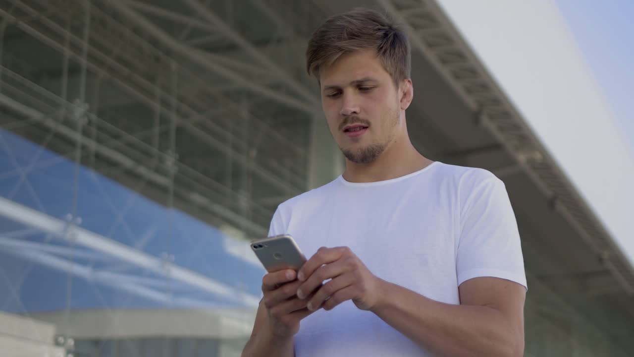 예쁜 젊은 남자가 스마트폰에서 앱을 사용하여 문자 메시지를 보내고 있습니다.