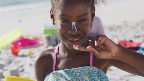 Video-of-happy-african-american-daughter-with-sunscreen-on-beach