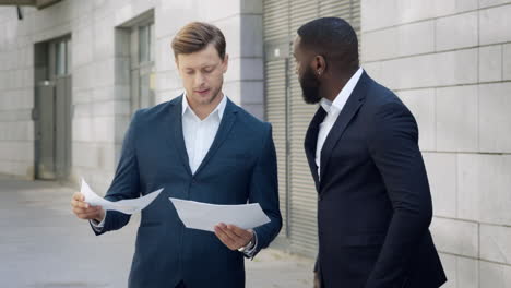 Businessmen-looking-at-documents-on-street.-Business-men-discussing-graphics