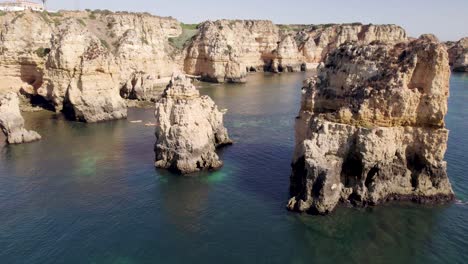 Emerald-ocean-calm-waters-with-eroded-rock-formations-and-cliffs-in-Lagos,-Algarve,-Portugal