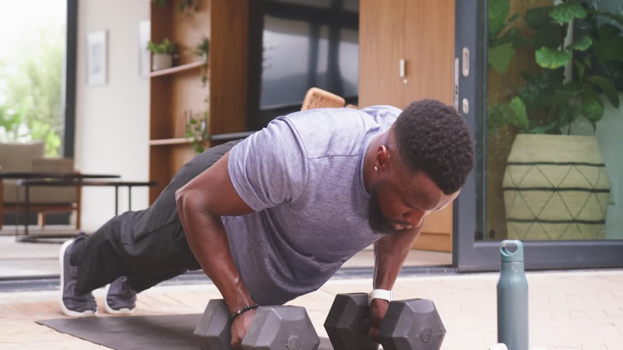 African American man in gray tee gripping hex weights lowering chest pressing at patio for strength