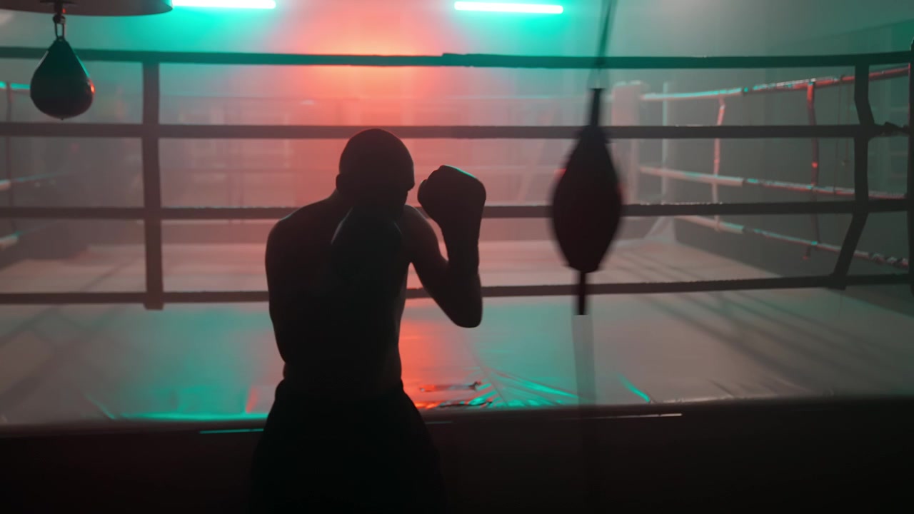 Silhouette eines männlichen Boxers beim Training mit einem Speed Bag in einem dunklen Fitnessstudio