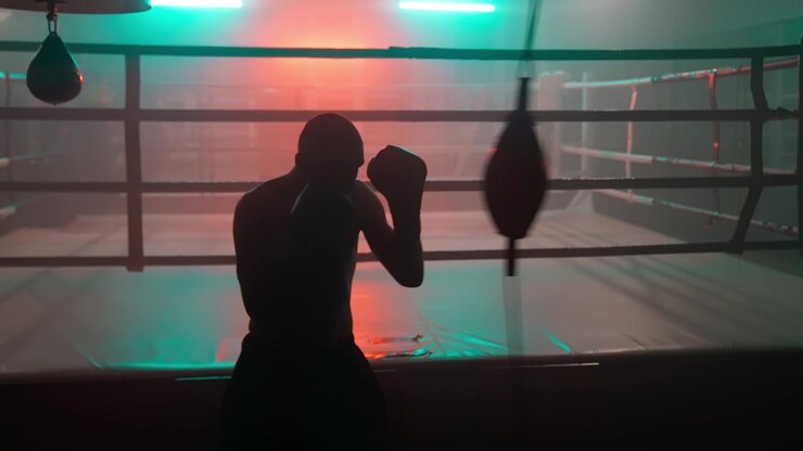 Silueta de boxeador masculino entrenando con un saco de velocidad en un gimnasio oscuro.