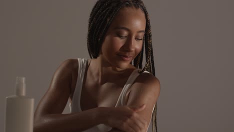 studio skincare beauty shot of young woman with long braided hair putting moisturiser onto arm and shoulder 2