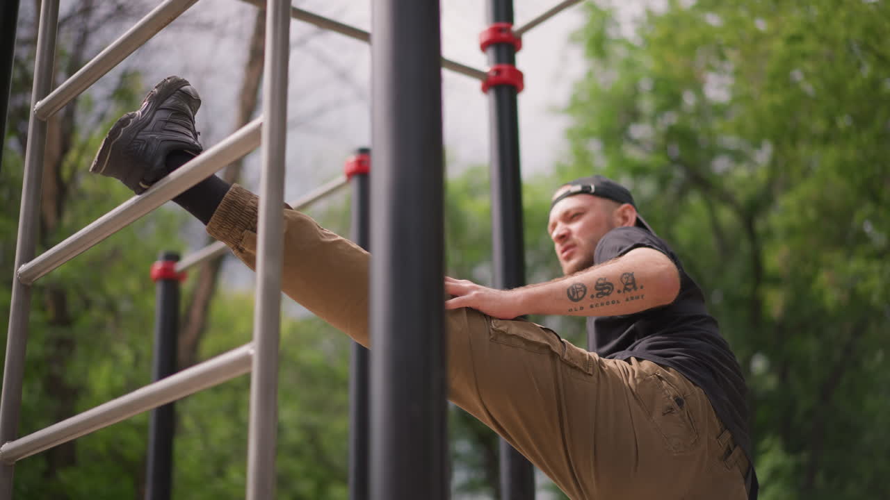 Man Stretching Outdoors, Person Demonstrating Flexibility Training Amid Lush Green Surroundings, Male Athlete Engaging In Stretching Sequence On Metal Bars In Scenic Outdoor Environment