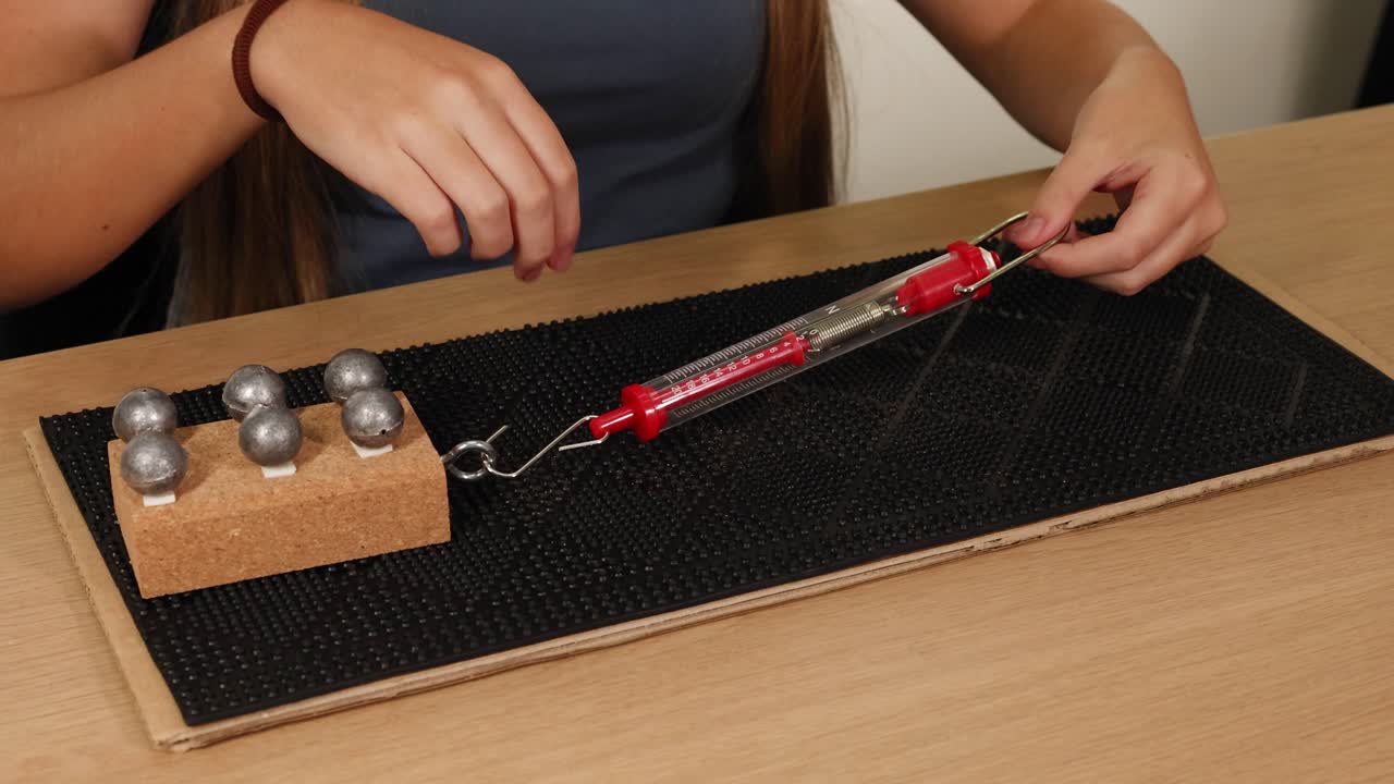 A person uses a spring scale to measure the force needed to drag a weighted block across a surface