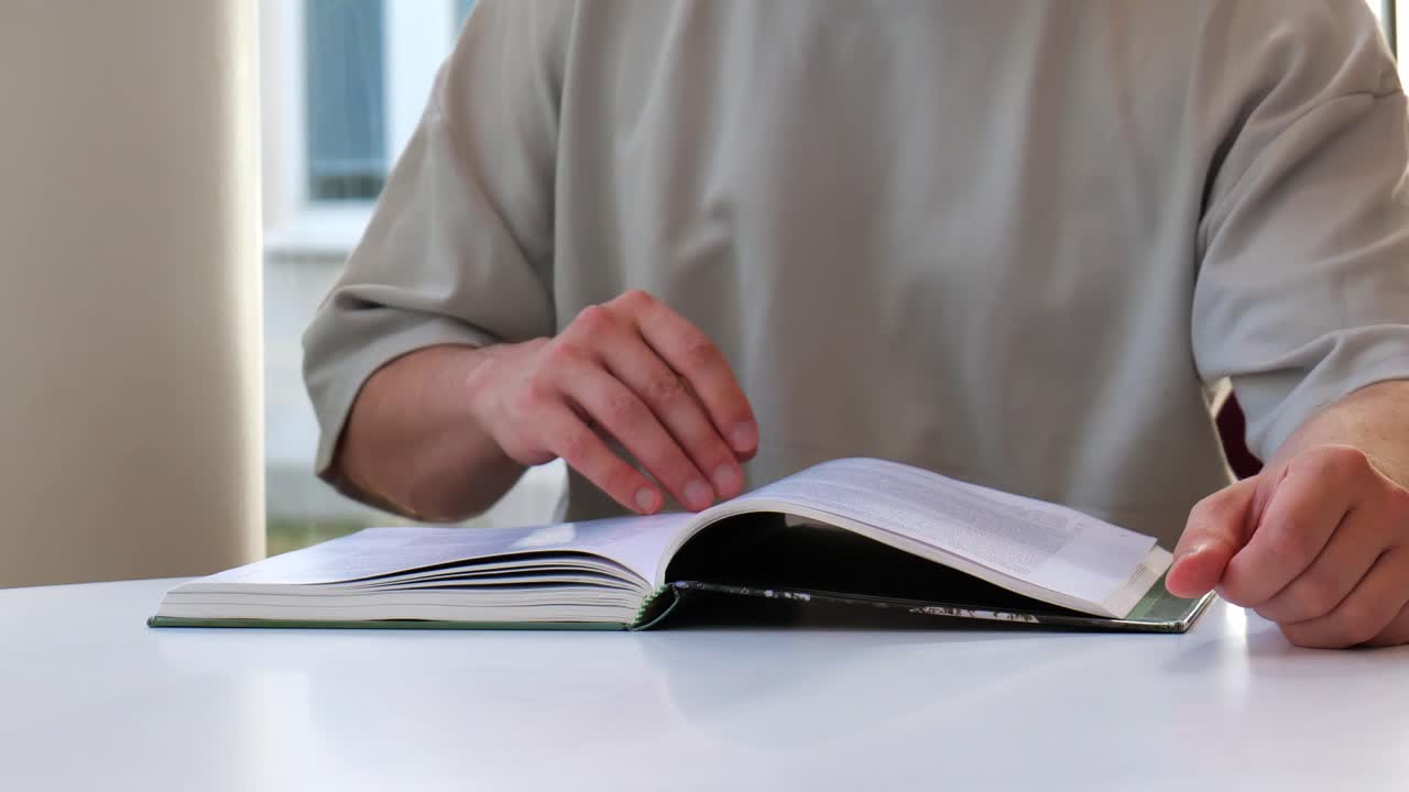 Man turning pages of a book slowly. Sitting on a table and studying while reading