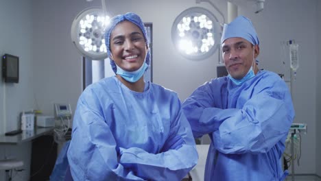 portrait of diverse male and female surgeon wearing lowered face masks smiling in operating theatre