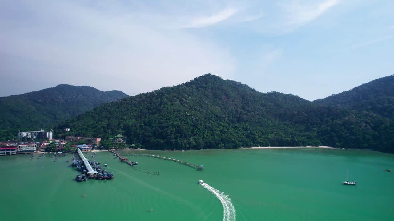 Drone shot of a boat gliding across the water, approaching a jetty in the distance