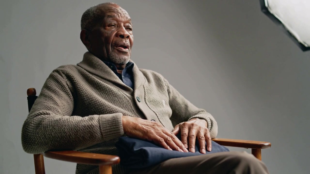 Adjusting senior man smoothing navy cloth on lap in studio responding to prompt, wearing cardigan
