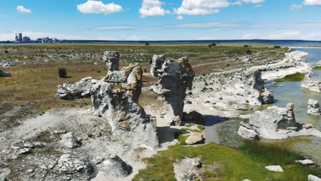 Aerial-birds-eye-drone-view-of-calm-Baltic-sea-and-interesting-rock-formation-in-coastline-of-Gotland-island-with-a-city-in-horizon