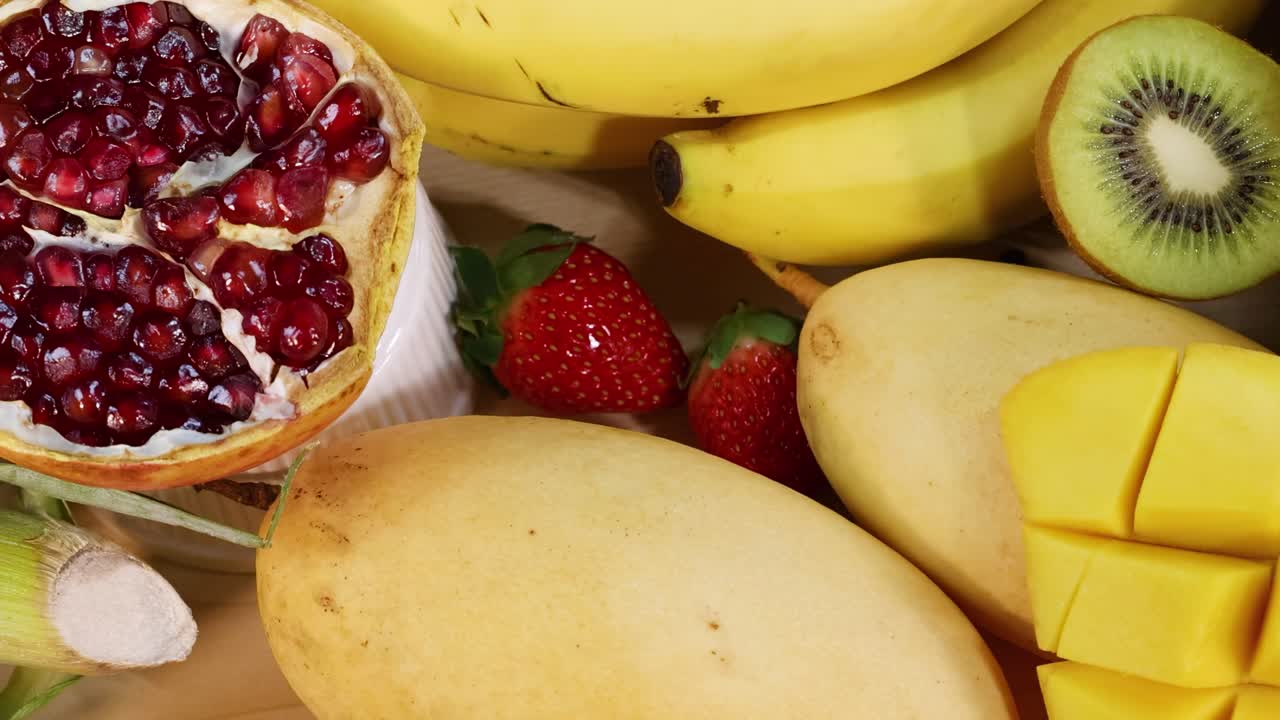 A colorful arrangement featuring bananas, mangoes, pomegranate halves, strawberries, and kiwi slices.