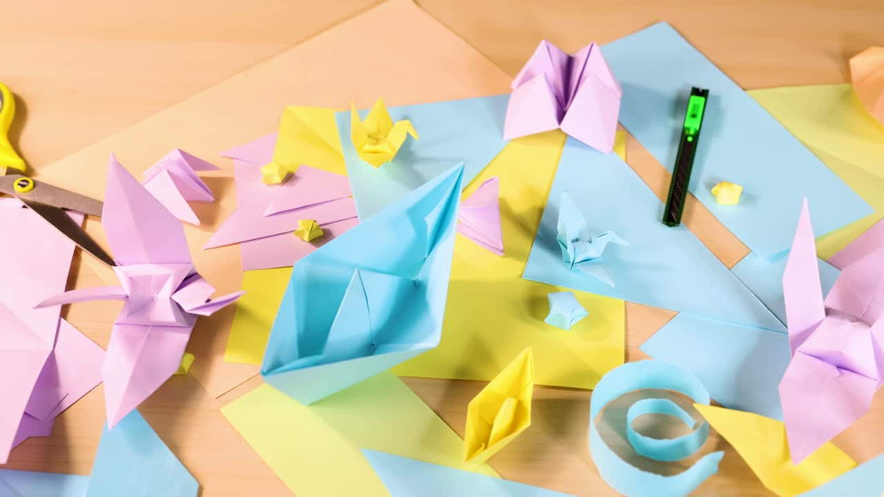 Assorted origami birds, boats, and shapes on pastel paper, bright lighting, overhead camera movement