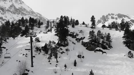 aerial view tracking along chairlift over snow-covered slopes and pine trees, ordino arcalis, andorra